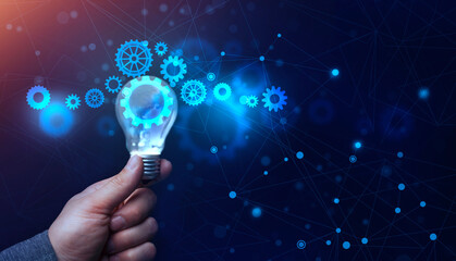 Businessman's Hand Holding Lightbulb With Working Holographic Cogwheels, Blue Background