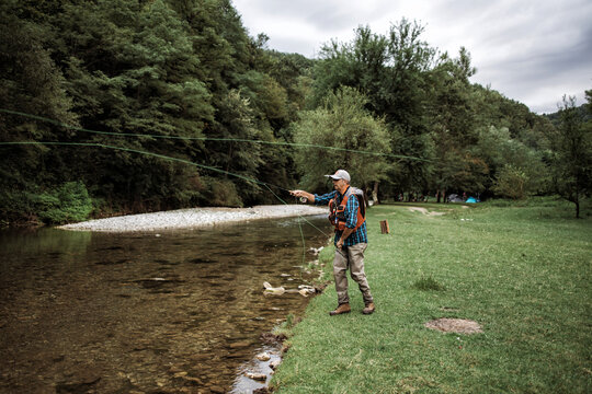 Senior man is fishing alone on fast mountain river. Active people and sport fly fishing concept. - a