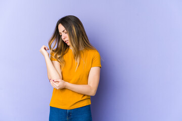 Young caucasian woman isolated on purple background massaging elbow, suffering after a bad movement.