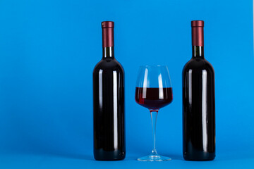 Two bottles of wine and a glass on a blue background. Space for text.