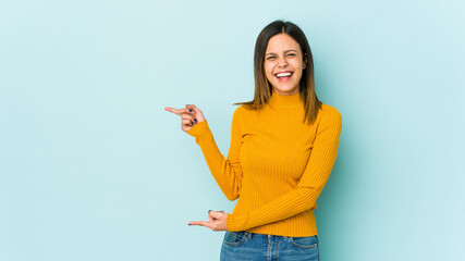 Young woman isolated on blue background pointing with forefingers to a copy space, expressing excitement and desire.
