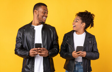 Cheerful African American Couple Using Smartphone Standing Over Yellow Background