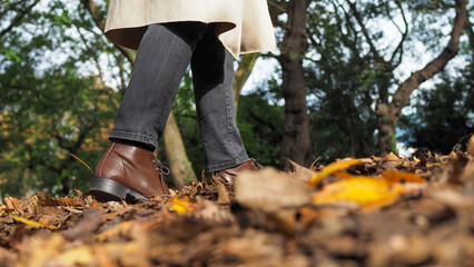 Closeup of a woman leather shoe walking inside the park and full of dry leaves on the floor. Selected focus.