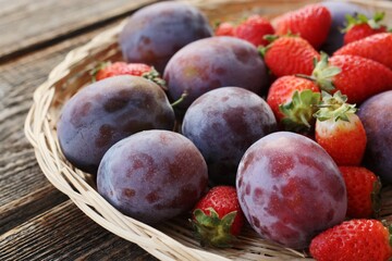 Ripe plums and strawberries on a wooden table