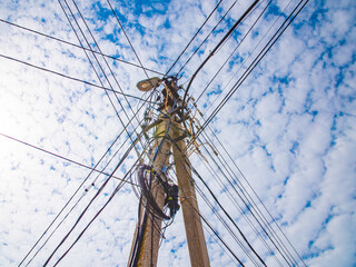 Fototapeta premium Electric lighting pole with wires on a background of blue sky with clouds. Lots of cables. Wire coil