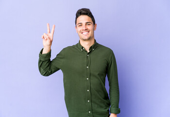 Fototapeta premium Young caucasian man isolated on purple background showing victory sign and smiling broadly.