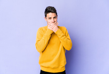 Young caucasian man isolated on purple background covering mouth with hands looking worried.