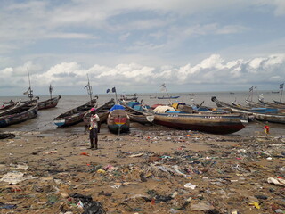 Freetown, Sierra Leone - July 5th 2019: fishing boats on the African coastline with plastic waste on the beach sand. Fishing and waste recycling context