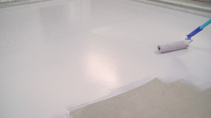 A worker paints the concrete floor with a roller white. Concrete Floor repair work. Paint roller in...