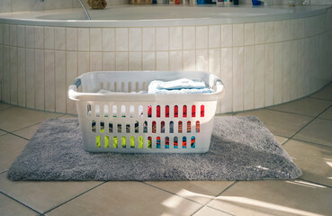 Plastik-Wäschekorb mit sauberer Wäsche steht auf dem  Teppich im Badezimmer 