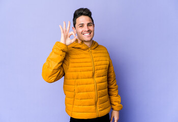 Young caucasian man isolated on purple background cheerful and confident showing ok gesture.