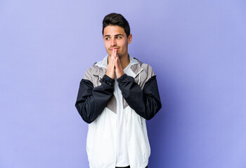 Young caucasian man isolated on purple background praying, showing devotion, religious person looking for divine inspiration.