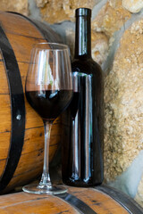 Glass of Red Wine and Dark Bottle on Wooden Barrel in Rustic Wine Cellar