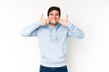 Naklejka premium Young man isolated on white background smiles, pointing fingers at mouth.