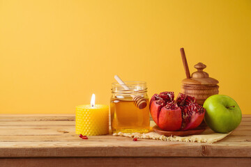 Jewish holiday Rosh Hashana concept with honey jar, apple and pomegranate on wooden table over yellow background