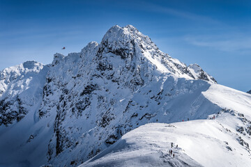 View from Kasprowy Wierch on adventurers climbing on Swinica mountain peak at winter. Tatra Mountains range with snow capped mountain peaks, Poland