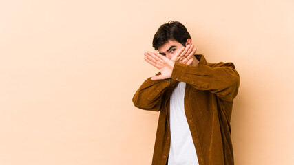 Young man isolated on beige background keeping two arms crossed, denial concept.