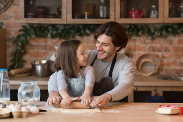 Cheerful young father and little daughter rolling dough for pizza together