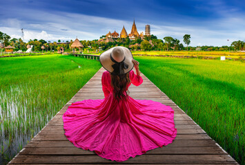 Thai female tourist sits on a wooden bridge looking at Wat Tham Sua in Kanchanaburi, Thailand.