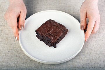 women's hands hold a white plate with a piece of brownie pie