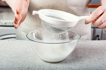 the chef's hands sift the flour through a sieve into a glass container