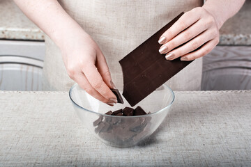 the chef's hands hold a bar of chocolate and break it into pieces in a glass bowl