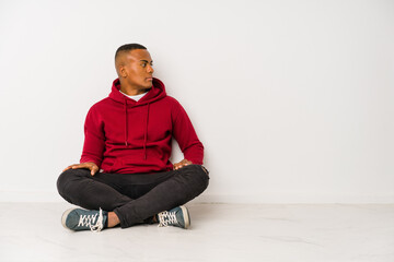 Young latin man sitting on the floor isolated gazing left, sideways pose.
