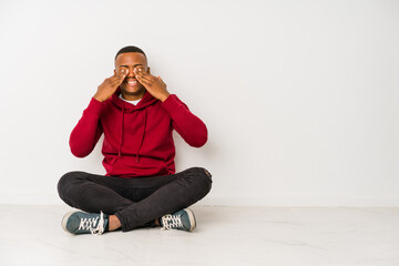 Young latin man sitting on the floor isolated covers eyes with hands, smiles broadly waiting for a surprise.