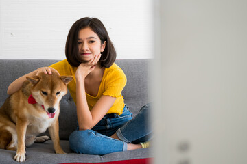 Happy woman and shiba inu dog sitting together on a sofa at home