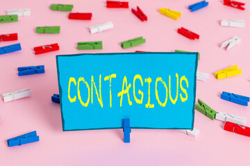 Text sign showing Contagious. Business photo showcasing transmissible by direct or indirect contact with infected an individual Colored clothespin papers empty reminder pink floor background office