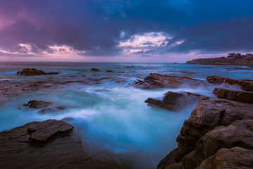 the power our oceans, closeup photography of the waves hitting into the rocks, and the water splashing up into the air during the sunset with beautiful cloudscape in the background 