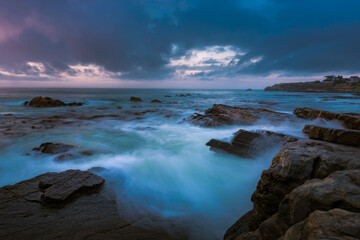 the power our oceans, closeup photography of the waves hitting into the rocks, and the water splashing up into the air during the sunset with beautiful cloudscape in the background 