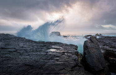 the power our oceans, closeup photography of the waves hitting into the rocks, and the water splashing up into the air during the sunset with beautiful cloudscape in the background 