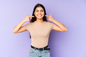 Young indian woman isolated on purple background smiles, pointing fingers at mouth.