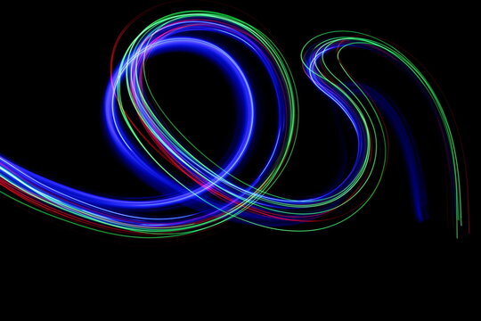 Long exposure photograph of neon blue colour in an abstract swirl, parallel lines pattern against a black background. Light painting photography