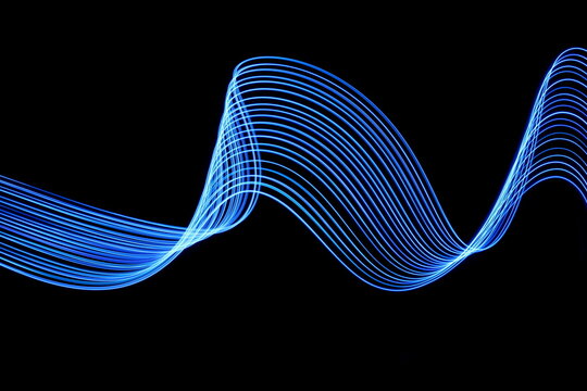 Long exposure photograph of neon blue colour in an abstract swirl, parallel lines pattern against a black background. Light painting photography