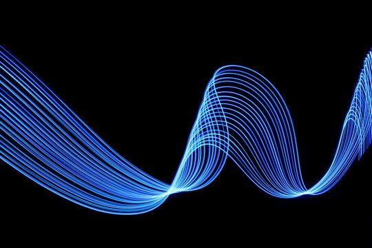 Long exposure photograph of neon blue colour in an abstract swirl, parallel lines pattern against a black background. Light painting photography