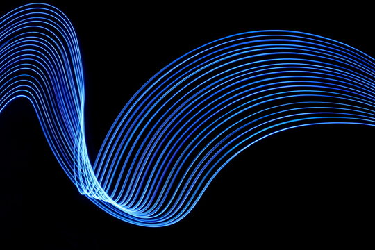 Long exposure photograph of neon blue colour in an abstract swirl, parallel lines pattern against a black background. Light painting photography