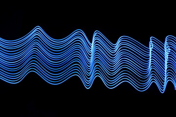 Long exposure photograph of neon blue colour in an abstract swirl, parallel lines pattern against a black background. Light painting photography