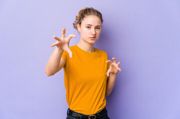 Young caucasian woman on purple background showing claws imitating a cat, aggressive gesture.