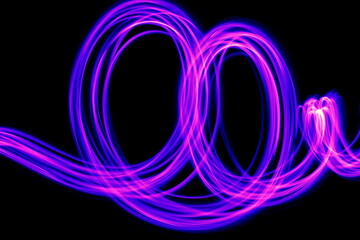 Long exposure photograph of purple neon colour in an abstract swirl, parallel lines pattern against a black background. Light painting photography.