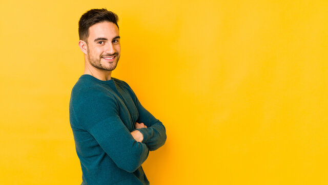 Young caucasian man isolated on yellow bakground who feels confident, crossing arms with determination.