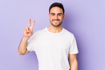Naklejka premium Young caucasian man isolated on purple background showing victory sign and smiling broadly.