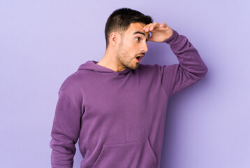 Obraz premium Young caucasian man isolated on purple background looking far away keeping hand on forehead.