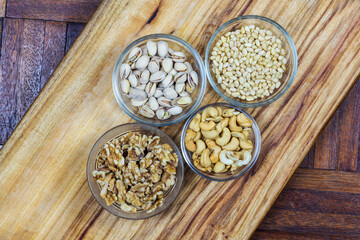 clear bowls with pistachio, walnuts, pine nuts and cashew on wooden background