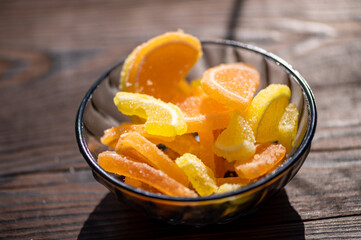 Marmalade lemon slices in a glass vase on a wooden table in the sunlight, close-up, selective focus.