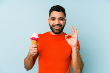 Young latin man holding an ice cream isolated cheerful and confident showing ok gesture.