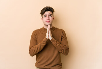 Fototapeta na wymiar Young caucasian man isolated on beige background holding hands in pray near mouth, feels confident.