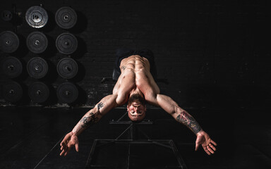 Young sweaty strong fit muscular man with big muscles doing abs workout on the bench in the gym as...