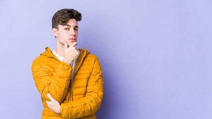 Young caucasian man isolated on purple background suspicious, uncertain, examining you.
